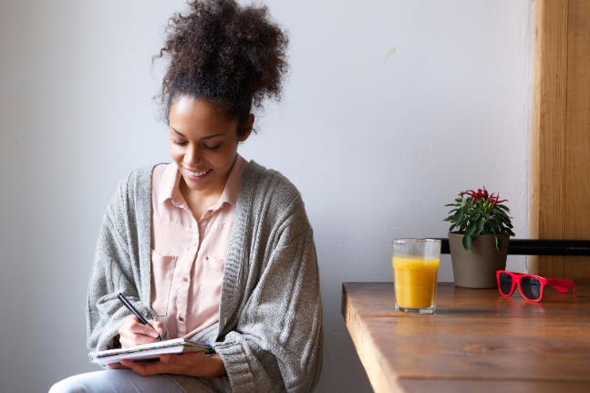 portrait of a smiling woman writing on note pad at home